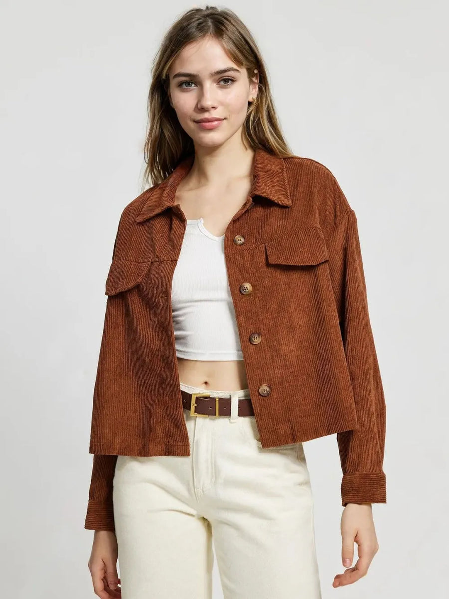 Woman wearing a brown corduroy jacket over a white top and beige pants on a light gray background