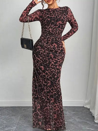 Woman wearing a leopard print dress with a black handbag against a white wall.