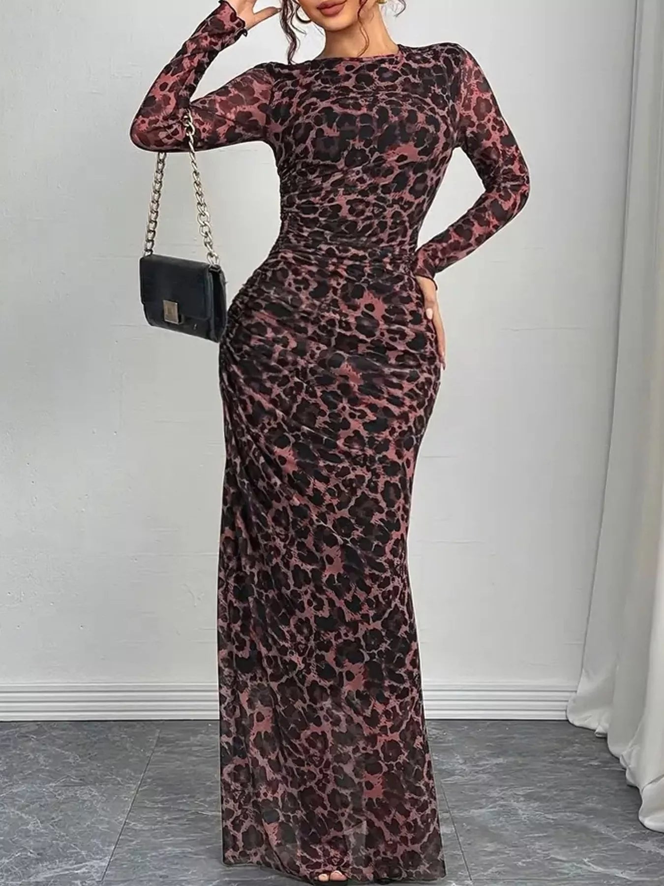 Woman wearing a leopard print dress with a black handbag against a white wall.