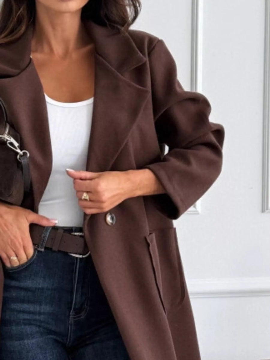 Person wearing a brown coat over a white top and blue jeans.