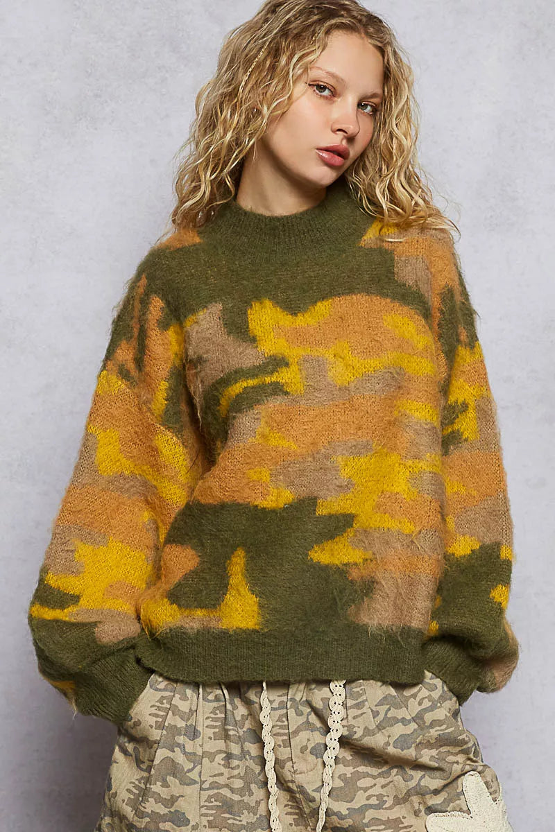 Person wearing a camouflage sweater and pants against a plain background
