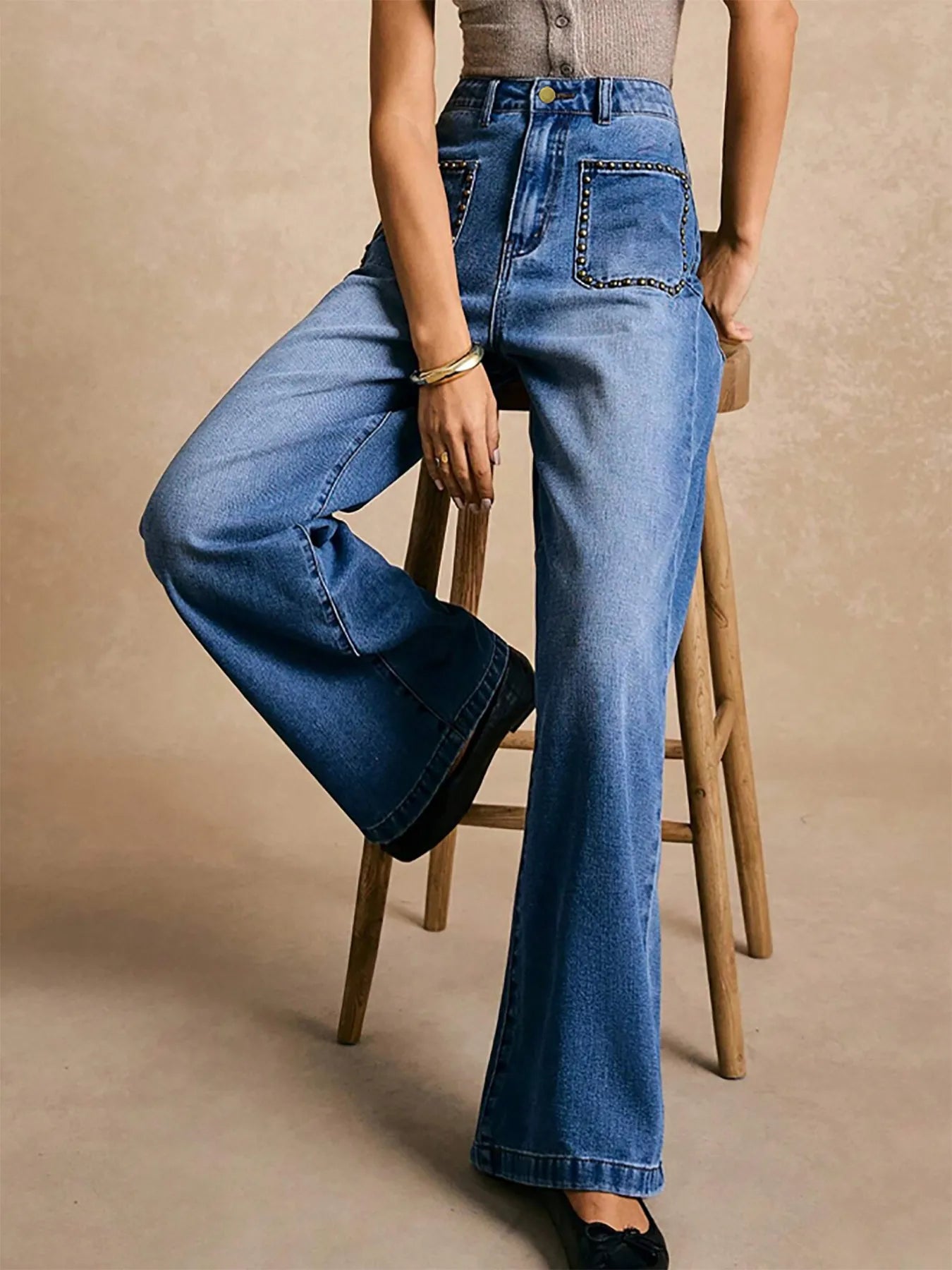 Person wearing blue jeans sitting on a wooden stool against a beige background