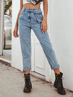Person wearing high-waisted blue jeans and black boots standing against a white wall.