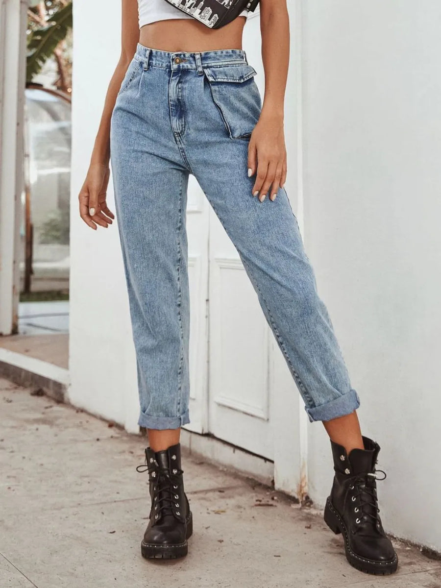 Person wearing high-waisted blue jeans and black boots standing against a white wall.
