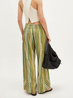 Person wearing green and yellow striped pants holding a black bag on a white background