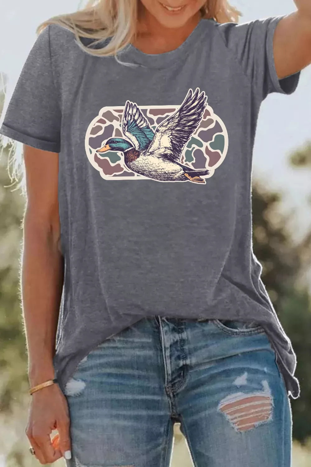 Person wearing a gray t-shirt with a duck graphic design outdoors