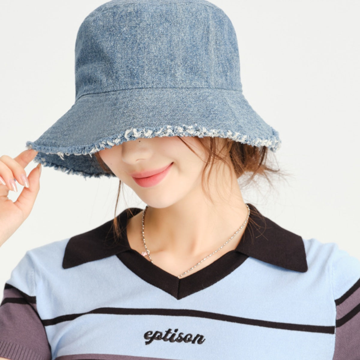 Person wearing a denim bucket hat with a plain background