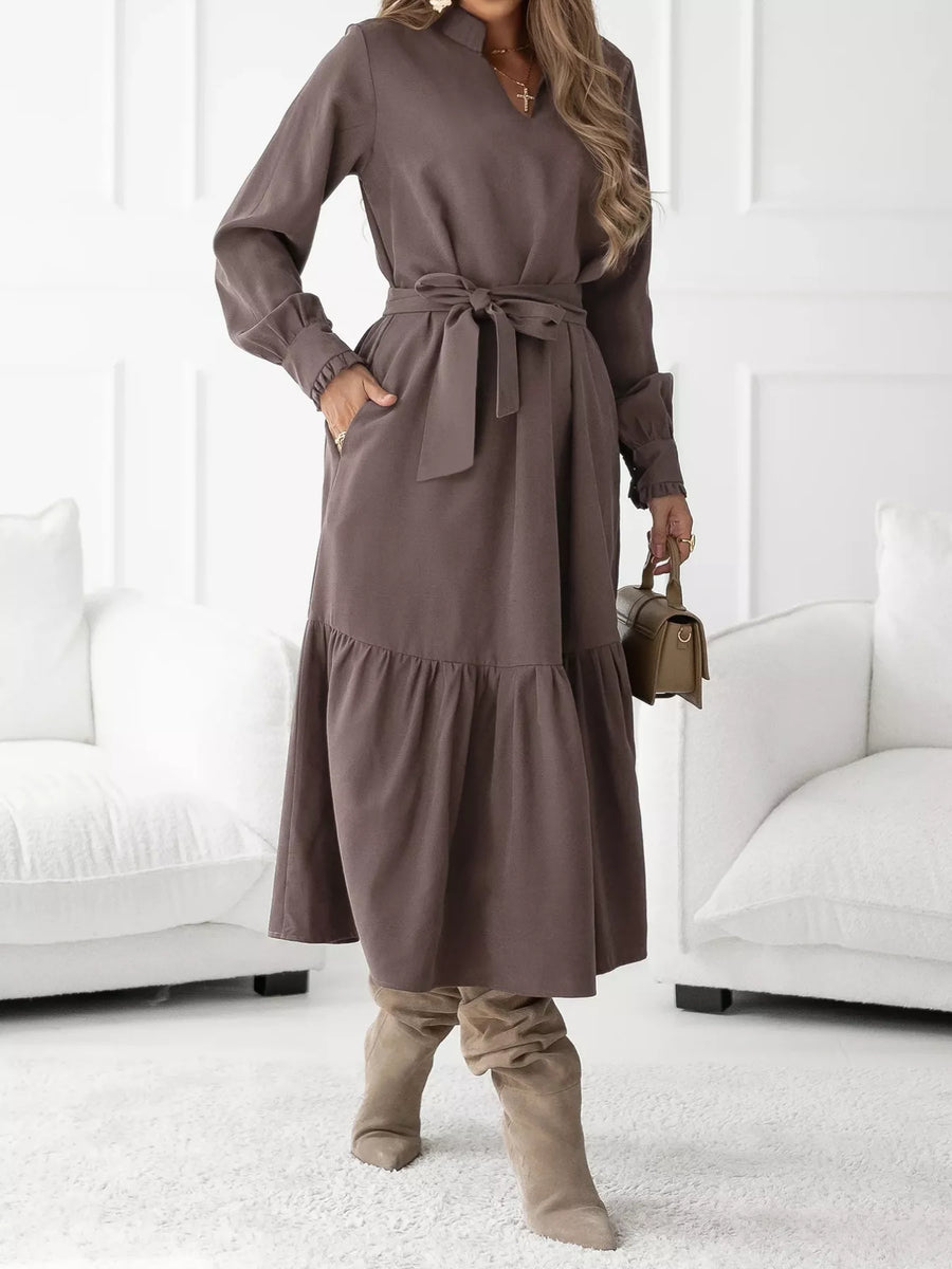Woman wearing a brown dress with a belt, standing in a minimalistic room.
