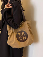 Beige tote bag with 'TELON' logo held by a person wearing a dark coat.