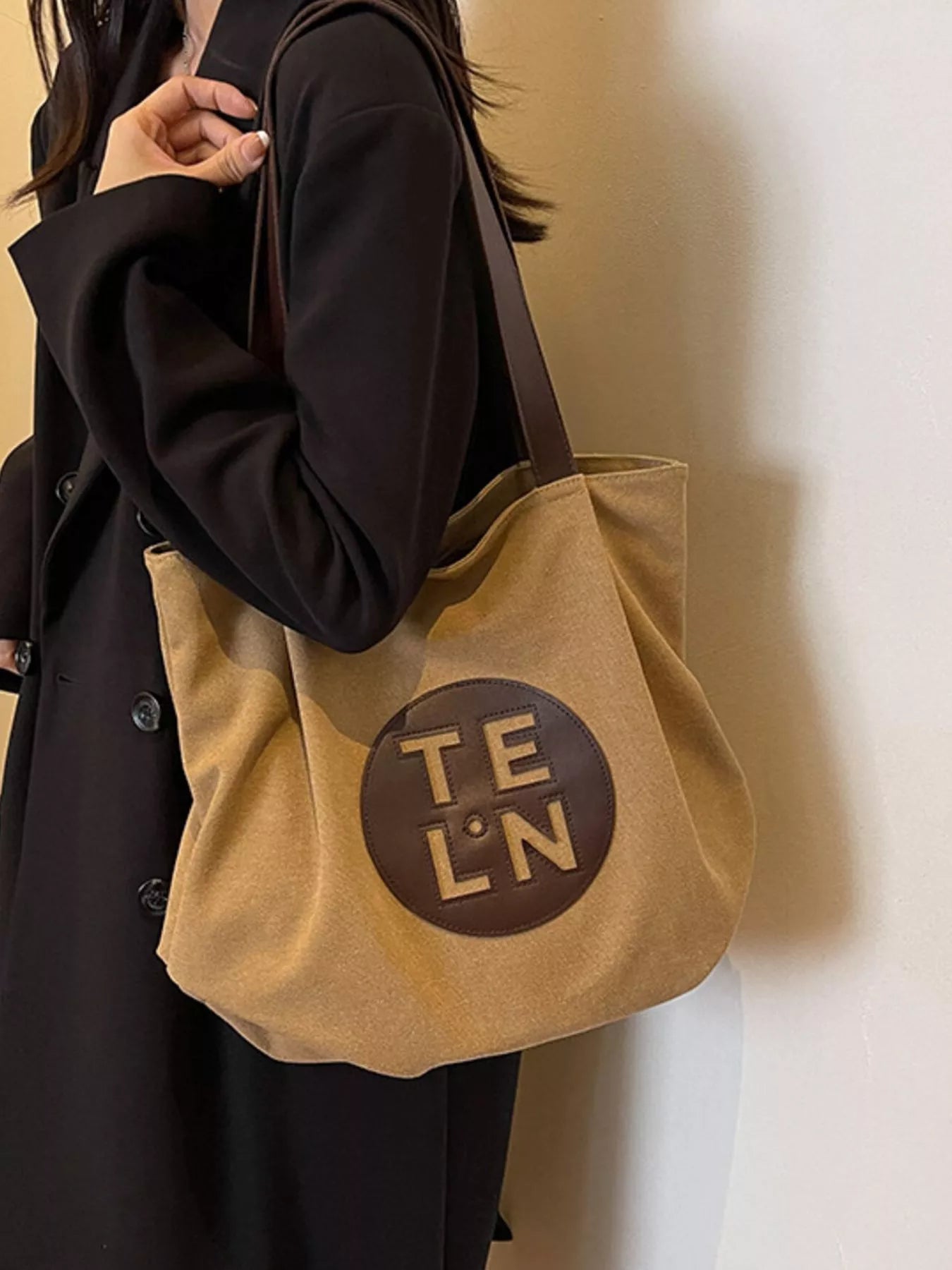Beige tote bag with 'TELON' logo held by a person wearing a dark coat.
