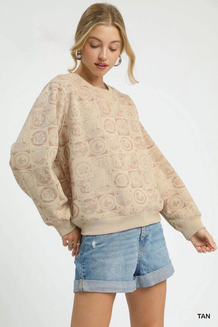 Woman wearing a beige patterned sweater and denim shorts on a white background