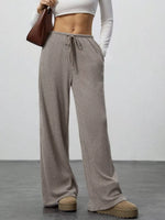 Person wearing brown wide-leg pants with a white top against a plain background