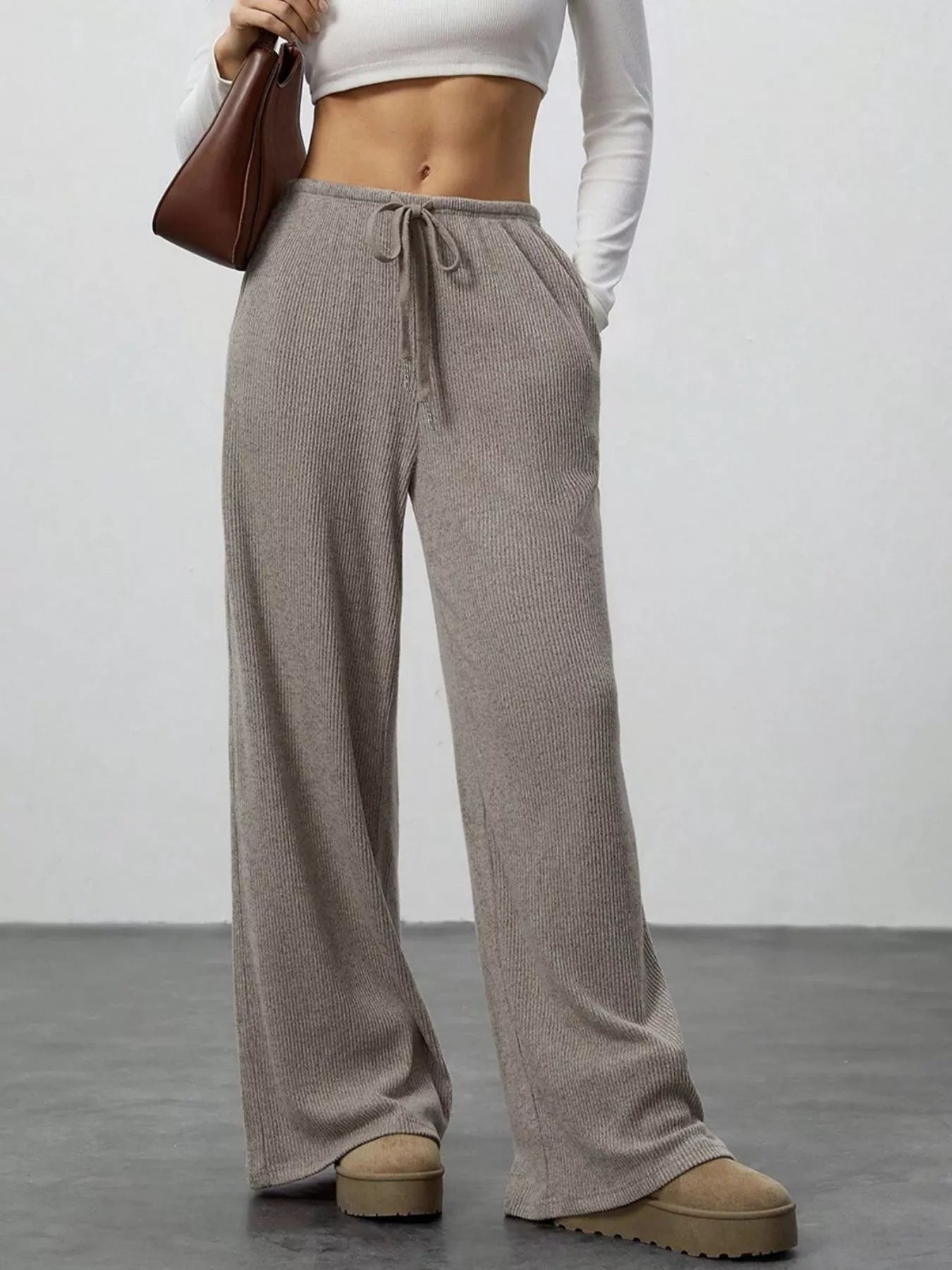 Person wearing brown wide-leg pants with a white top against a plain background
