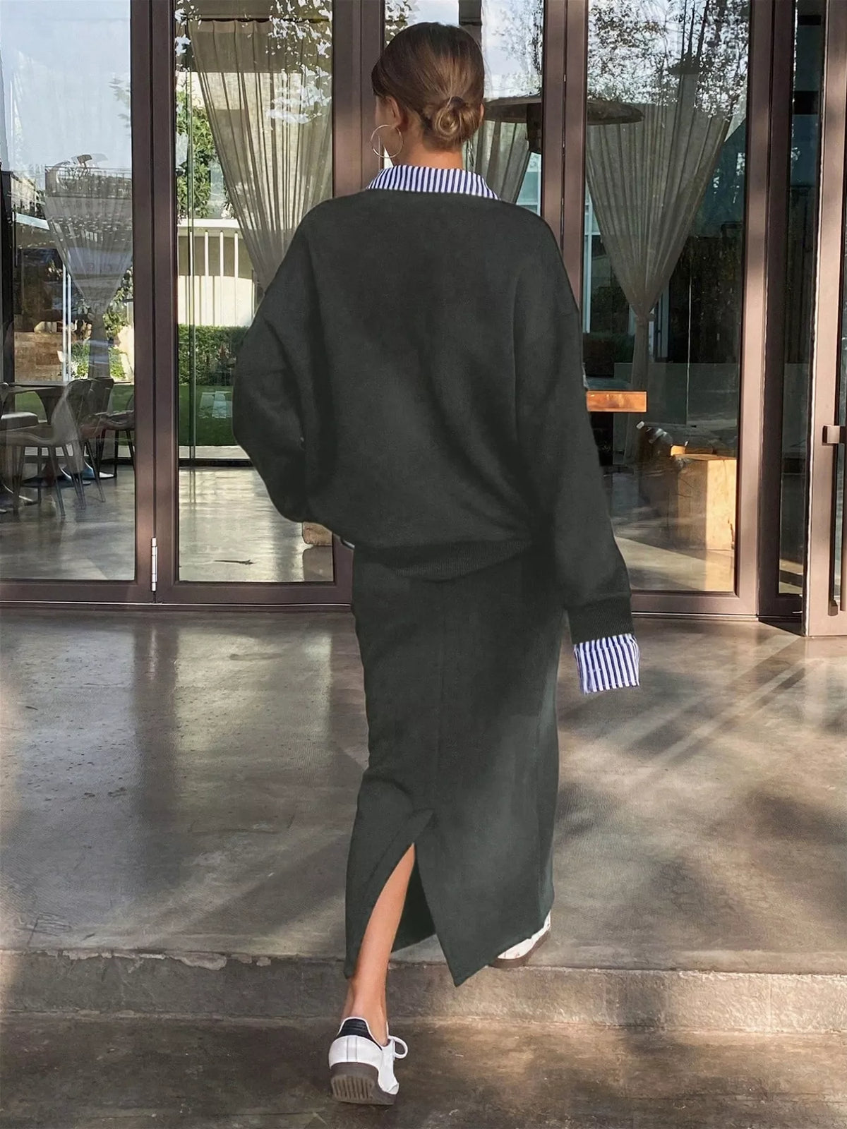 Person wearing a black outfit with a high slit walking towards large glass doors.