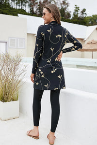 Woman wearing a black floral dress on a rooftop with a white building and greenery in the background.