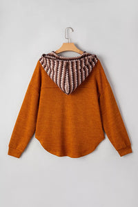 Brown sweater with a patterned hood on a wooden hanger against a light gray background