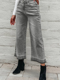 Person wearing gray wide-leg jeans against a stone wall.