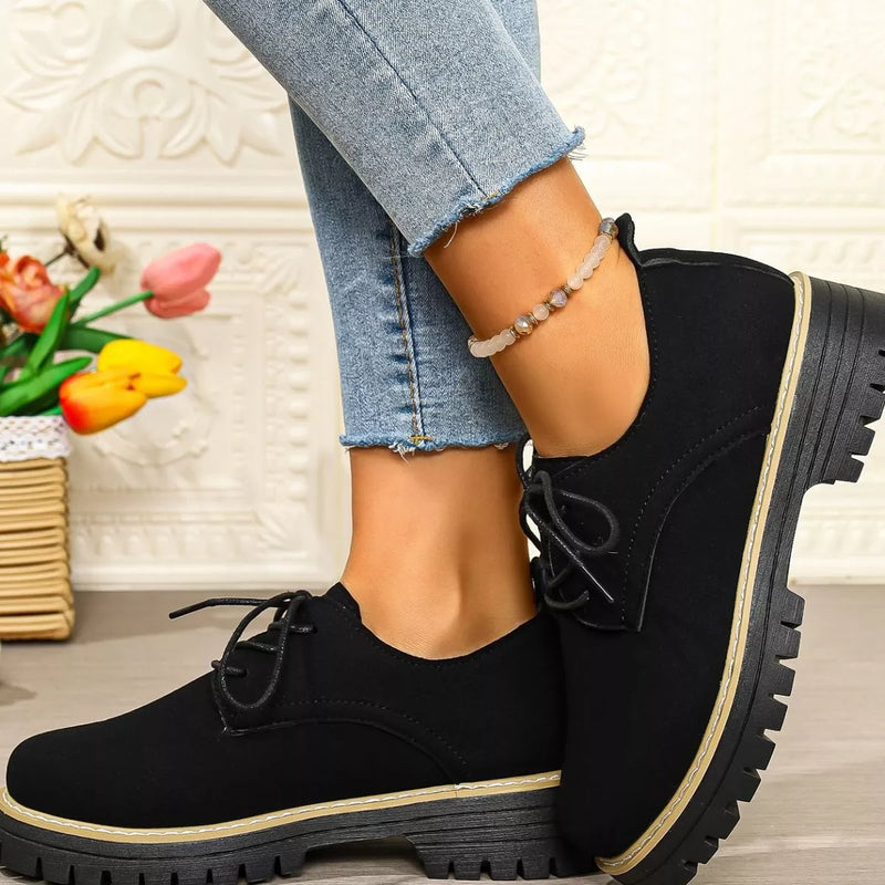 Black shoes with thick soles worn by a person, with a decorative background.
