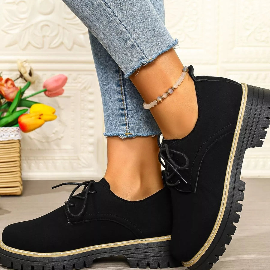 Black shoes with thick soles worn by a person, with a decorative background.