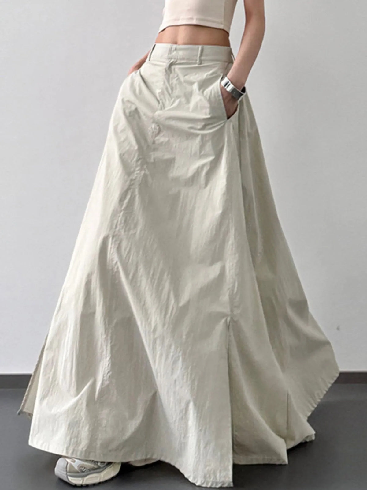 Person wearing a long light-colored skirt with a plain background