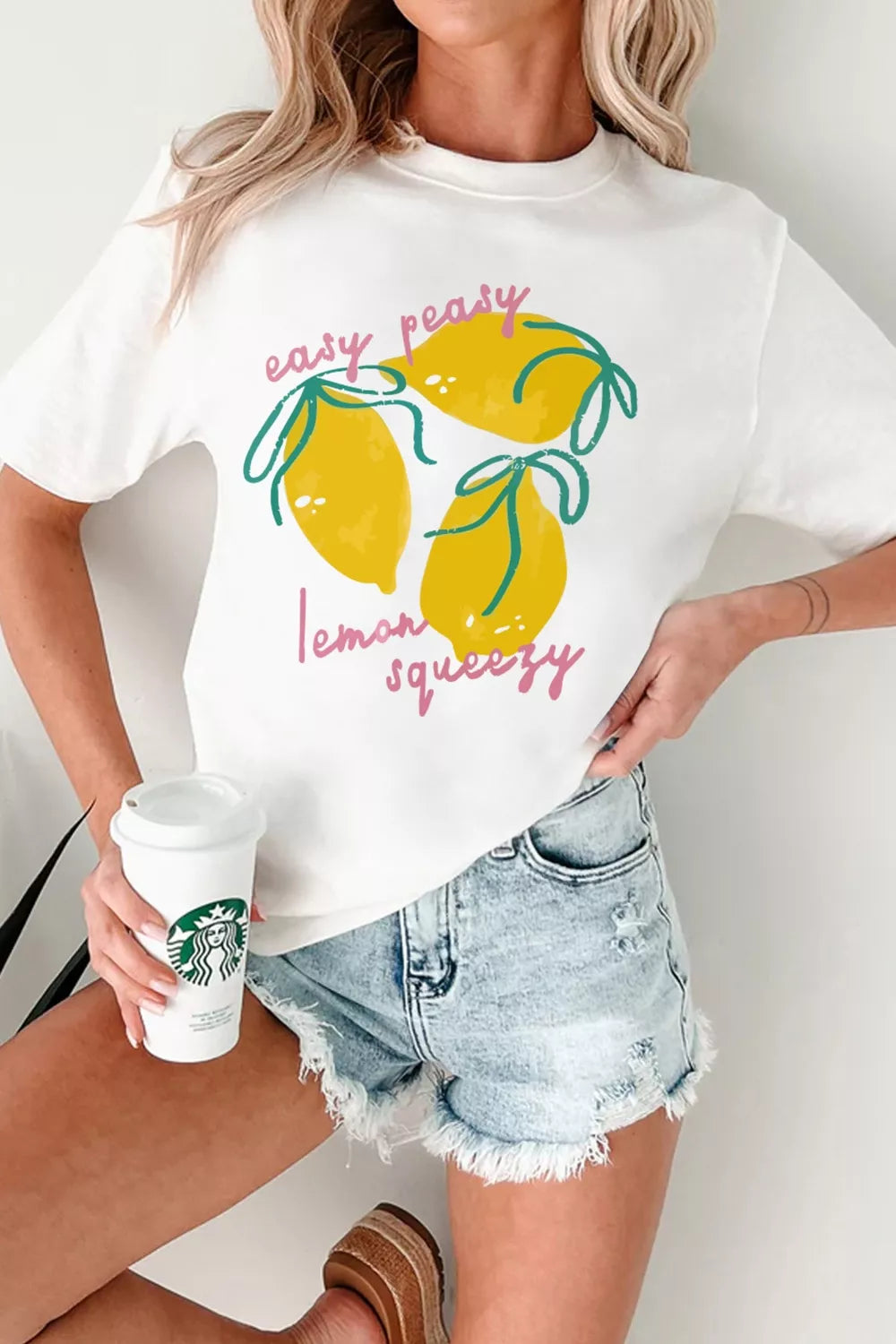 Person wearing a white t-shirt with lemon graphic and text, holding a Starbucks cup.