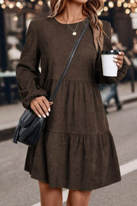Woman in a brown dress holding a coffee cup and a black handbag on a street.