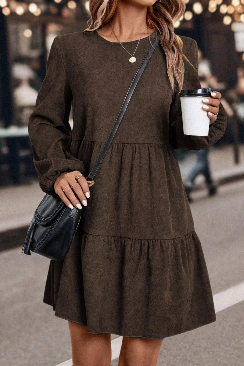 Woman in a brown dress holding a coffee cup and a black handbag on a street.