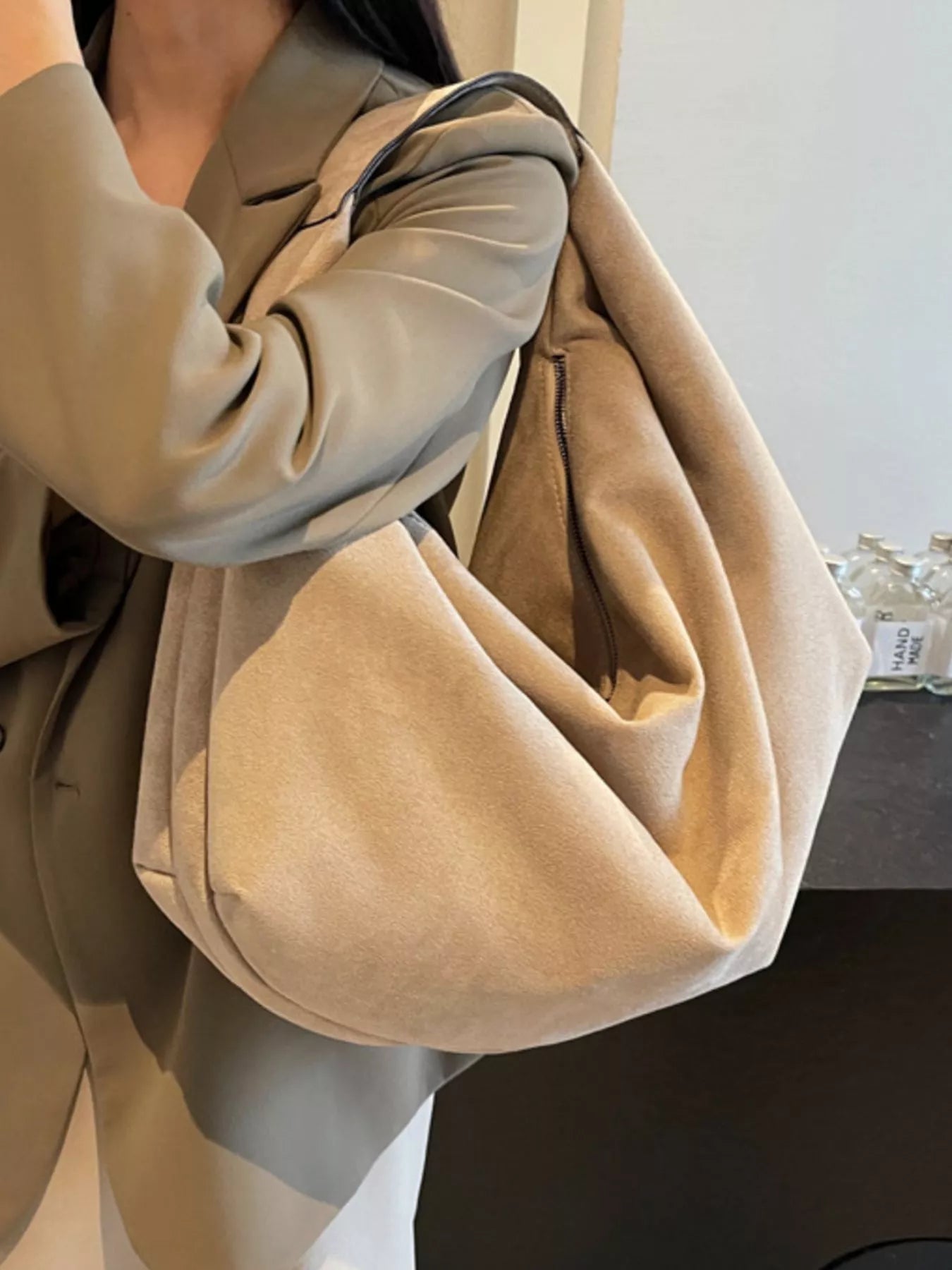 Beige handbag held by a person wearing a beige coat.