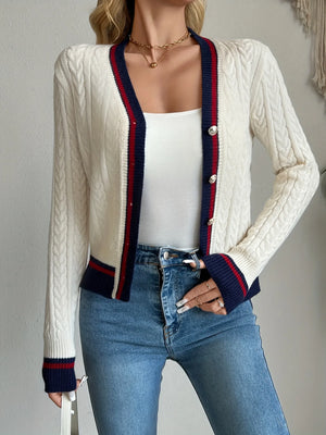 Woman wearing a white cable knit cardigan with red and blue trim, white top, and blue jeans.