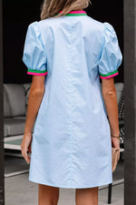 Light blue dress with pink and green trim worn by a person, standing indoors.