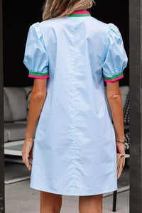 Light blue dress with pink and green trim worn by a person, standing indoors.