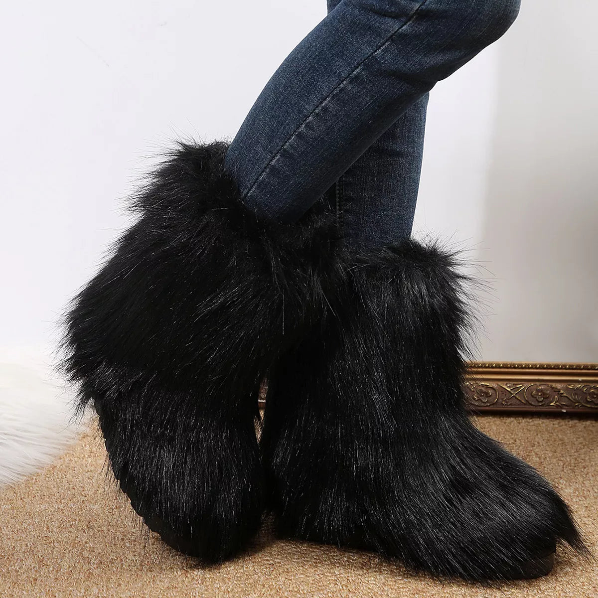 Black furry boots worn with blue jeans on a neutral background