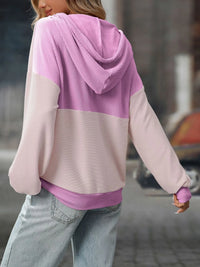 Person wearing a pink and light pink hoodie with a blurred background