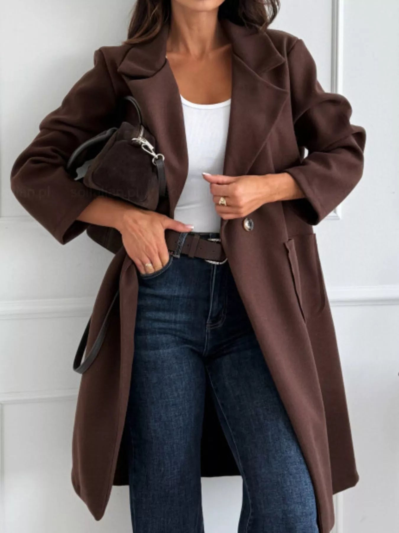 Person wearing a brown coat, white top, and blue jeans against a white background