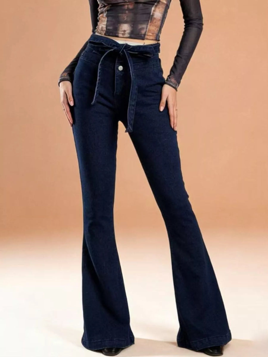 Dark blue flared jeans worn by a person on a beige background