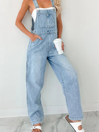 Person wearing light blue denim overalls against a white background