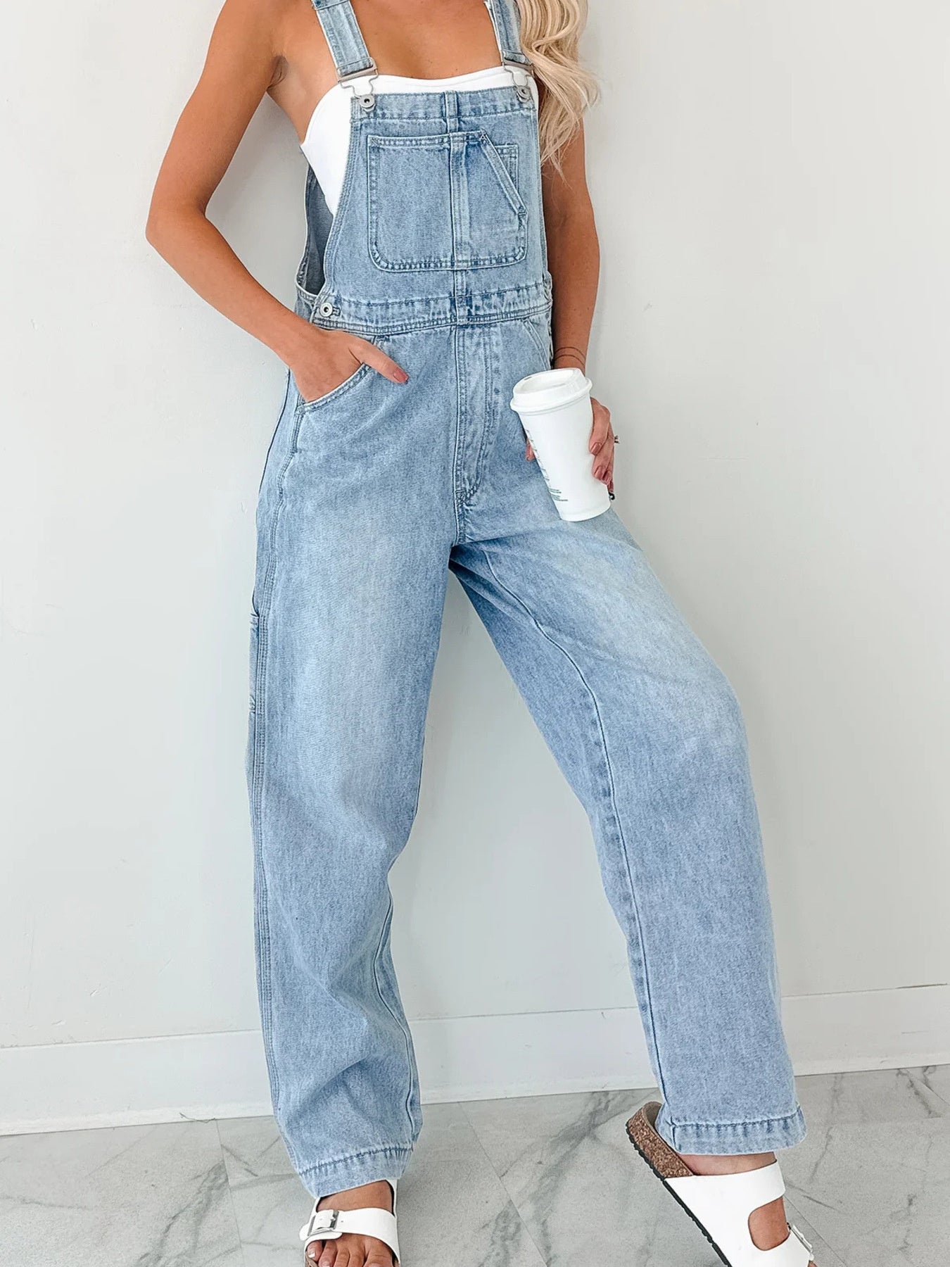 Person wearing light blue denim overalls against a white background
