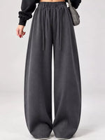 A person wearing dark charcoal gray wide-leg sweatpants with an elastic drawstring waist, styled with a black long-sleeve top and a gray shoulder bag against a light gray studio background.