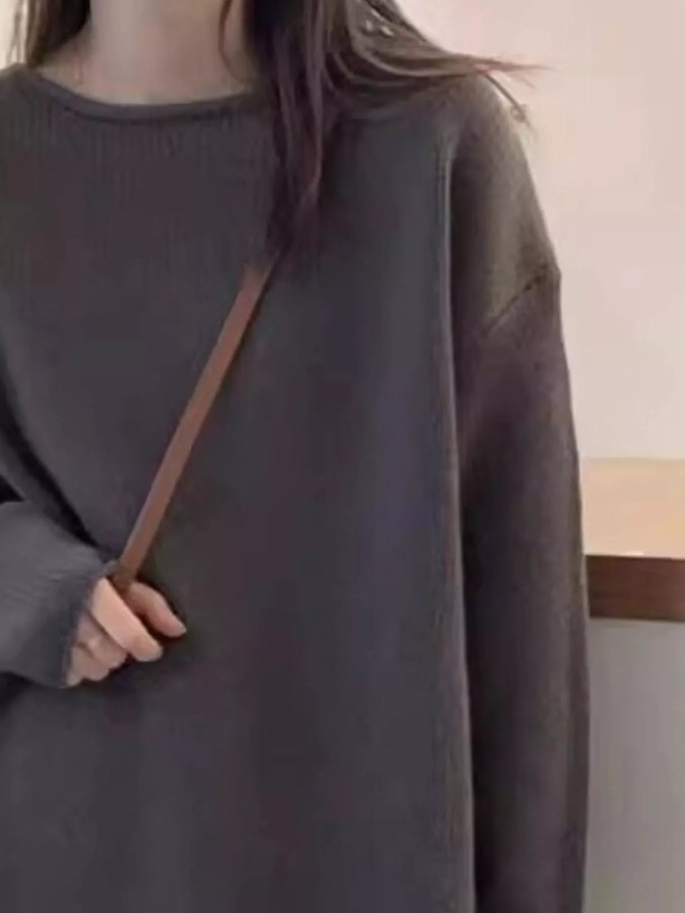 Person wearing a dark gray oversized sweater with a brown strap over the shoulder.