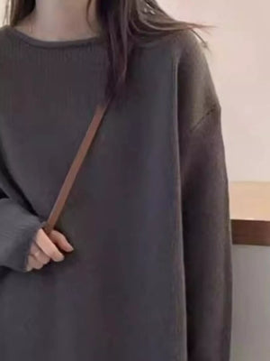 Person wearing a dark gray oversized sweater with a brown strap over the shoulder.