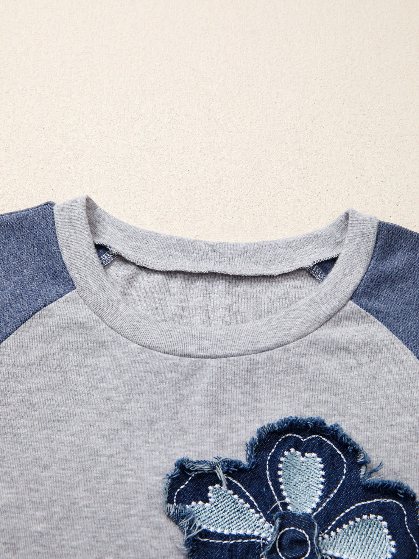 Close-up of a gray and blue children's shirt with a floral design on a beige background
