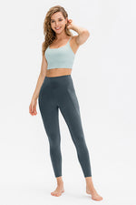 Woman wearing a light blue sports bra and dark gray leggings on a white background