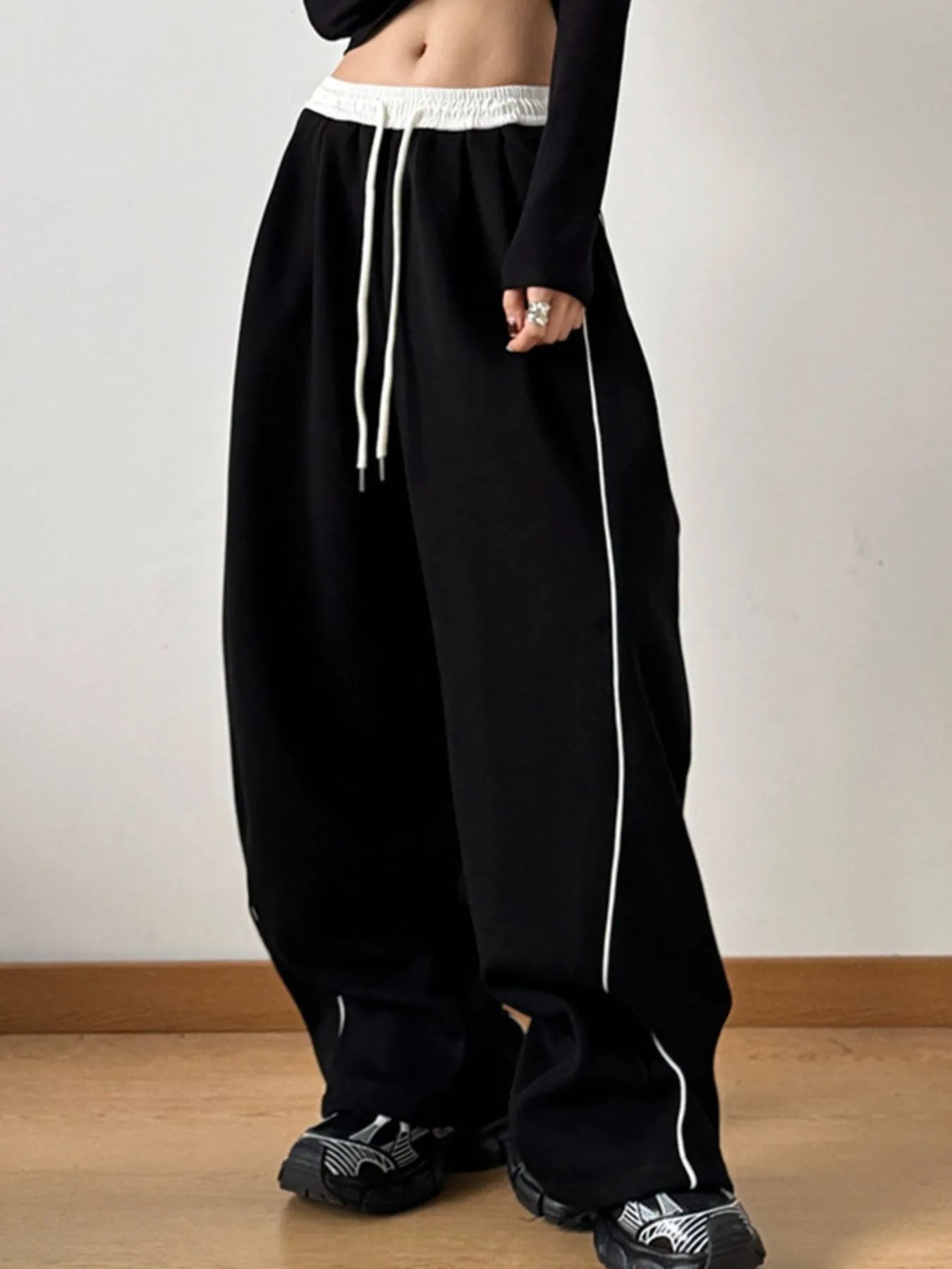 Person wearing black wide-leg pants with white drawstrings on a plain background