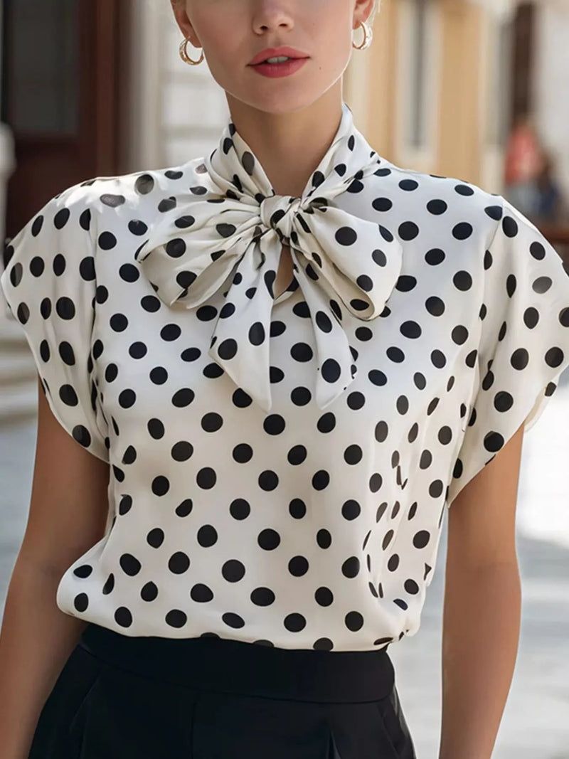 Woman wearing a polka dot blouse with a bow tie neckline.