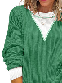 Green sweater with white trim worn by a person on a white background