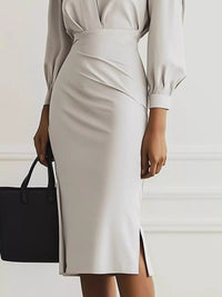 Person wearing a beige dress holding a black handbag against a white background