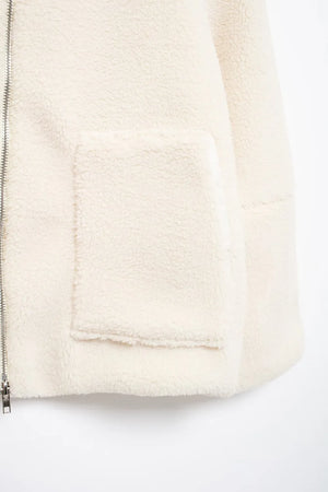 Close-up of a cream-colored fleece jacket with a zipper on a white background