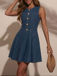 Woman wearing a blue denim dress with gold buttons against a neutral background