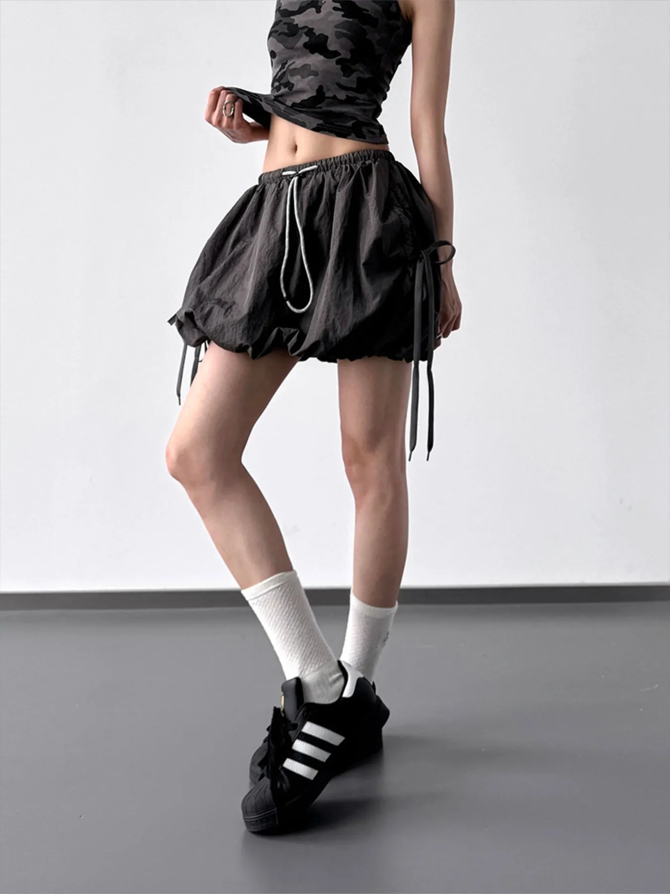 Person wearing black athletic shorts, white socks, and black sneakers on a plain background