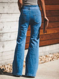 Person wearing blue jeans standing against a wooden wall.